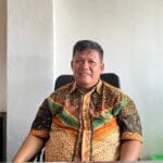Pria mengenakan batik duduk di kursi.