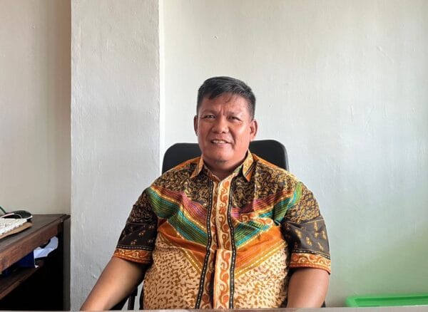 Pria mengenakan batik duduk di kursi.