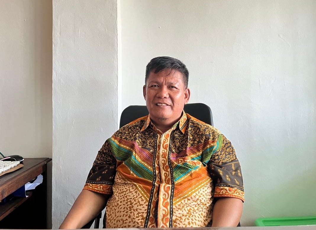 Pria mengenakan batik duduk di kursi.